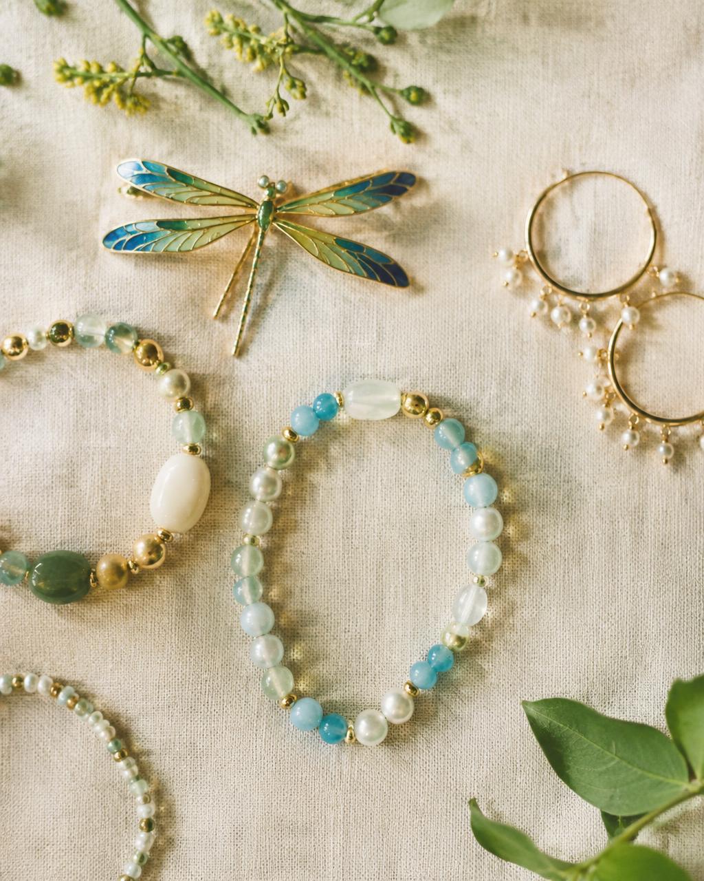 Enamel dragonfly brooch, beaded bracelets and pearl hoops on linen